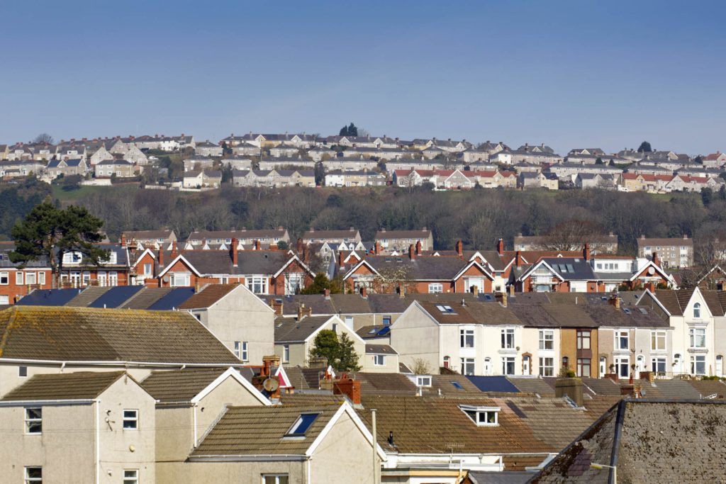 Image of hundreds of terraced houses with brown roofs and white walls with blue sky in the background